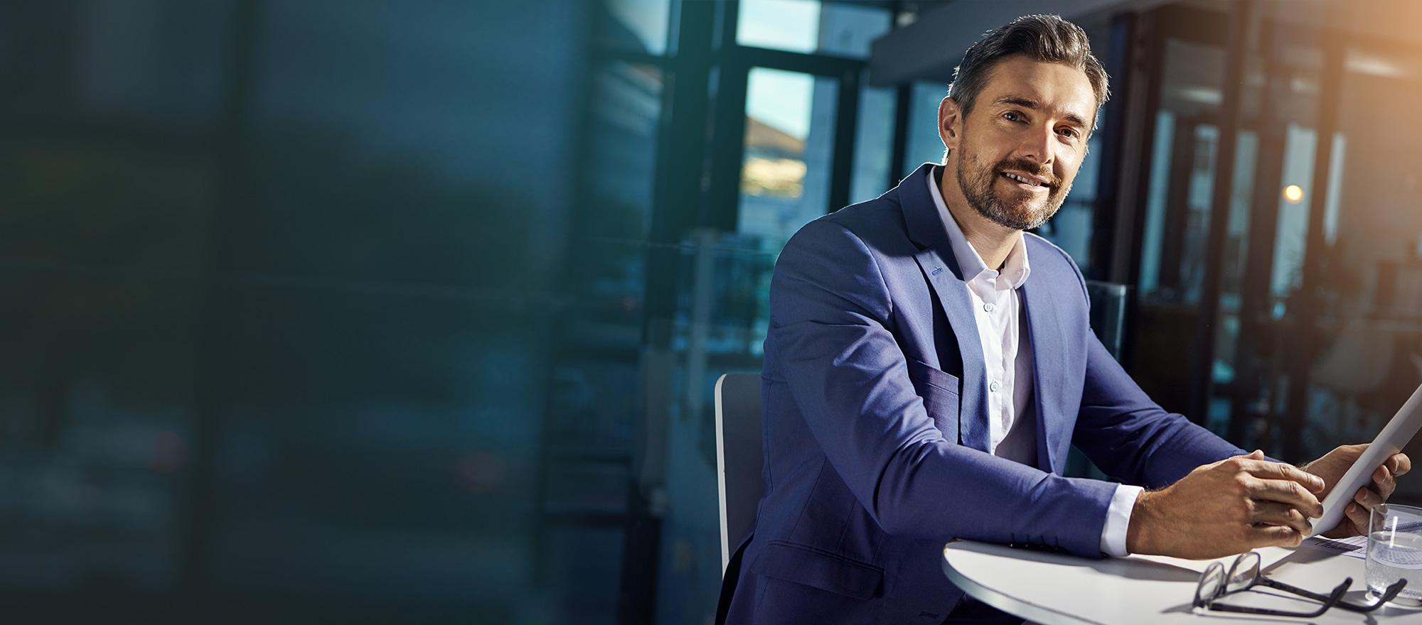 Man wearing a sports jacket with collared shirt sitting at desk with laptop open with CentralSquare Solutions on screen